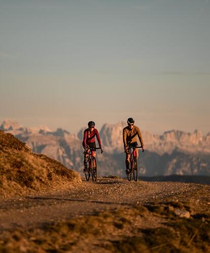 Zwei Radfahrer stehen mit ihren Fahrrädern auf einem Bergweg und blicken auf ein